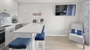 Een moderne keuken met witte kastjes, een marmeren aanrecht en blauwe barstoelen.