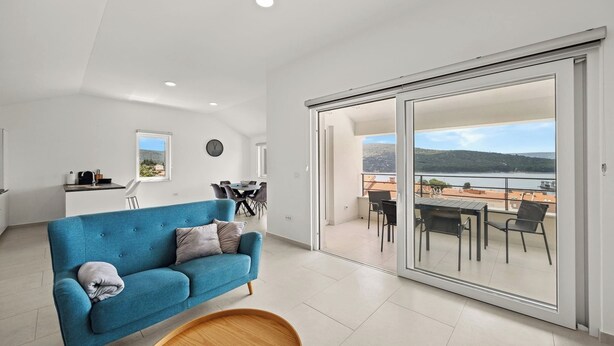 A modern living room with a blue sofa, a wooden coffee table, and a dining area with a table and chairs. - Enchanting Summer Apartment with Sea View (Cres)