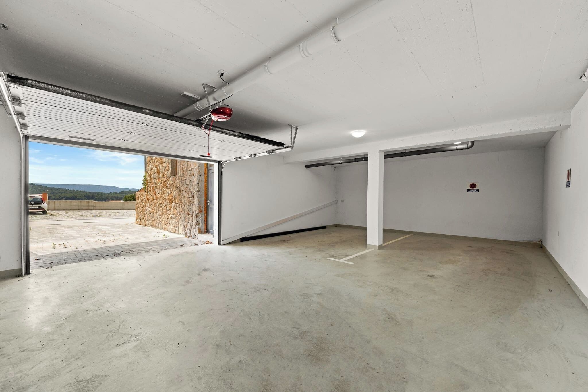 Uma garagem espaçosa com piso de concreto, uma grande porta aberta para o exterior e uma parede de pedra.