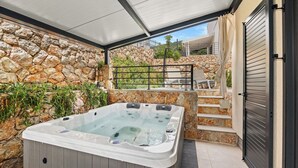A hot tub in a covered outdoor area with stone walls, a table, and a staircase leading to an upper level. - Couple's Vacation with Jacuzzi - Crepsa Paradise (Cres)
