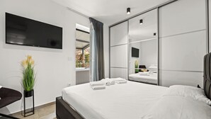 A modern hotel room with a large bed, a flat-screen TV, a desk, and a potted plant. - Couple's Vacation with Jacuzzi - Crepsa Paradise (Cres)