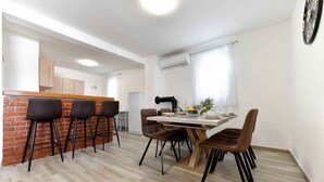 Uma cozinha moderna com parede de tijolos decorativa, uma área de jantar com mesa de madeira e cadeiras marrons, e um balcão com banquetas.