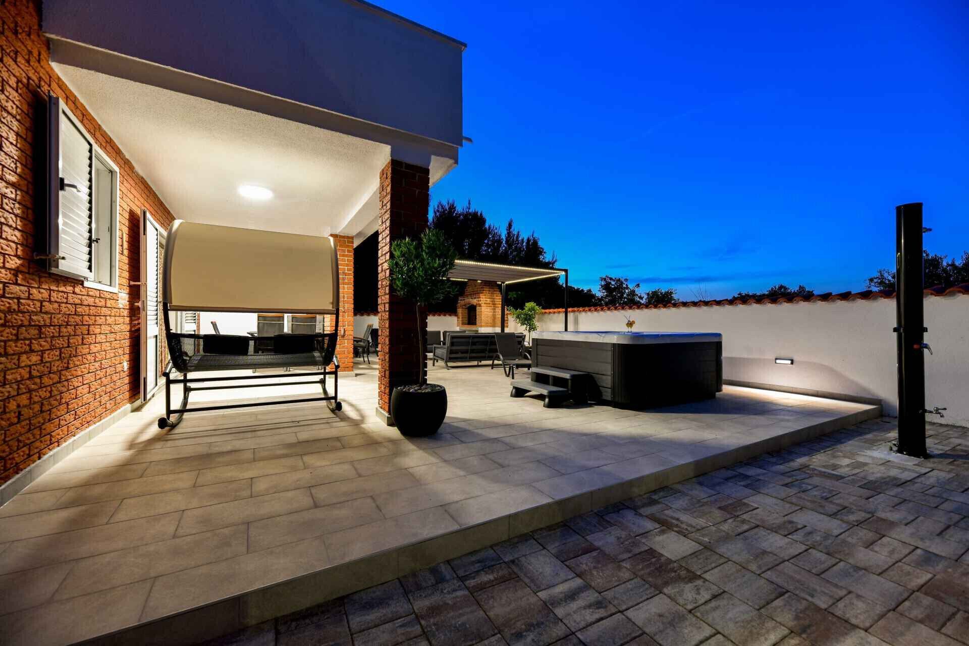 En udendørs terrasse med grill, siddepladser og jacuzzi.