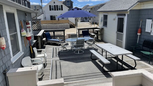 A patio area with a table, chairs, and a blue umbrella. - Cozy cabin less than 100 steps to the sand! (Hampton)