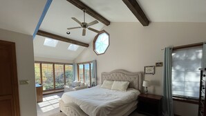 Une chambre spacieuse dotée d’un grand lit, d’un ventilateur de plafond et de nombreuses fenêtres qui laissent entrer la lumière naturelle.