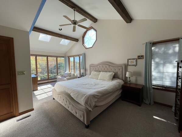 A spacious bedroom with a large bed, a ceiling fan, and multiple windows providing natural light.