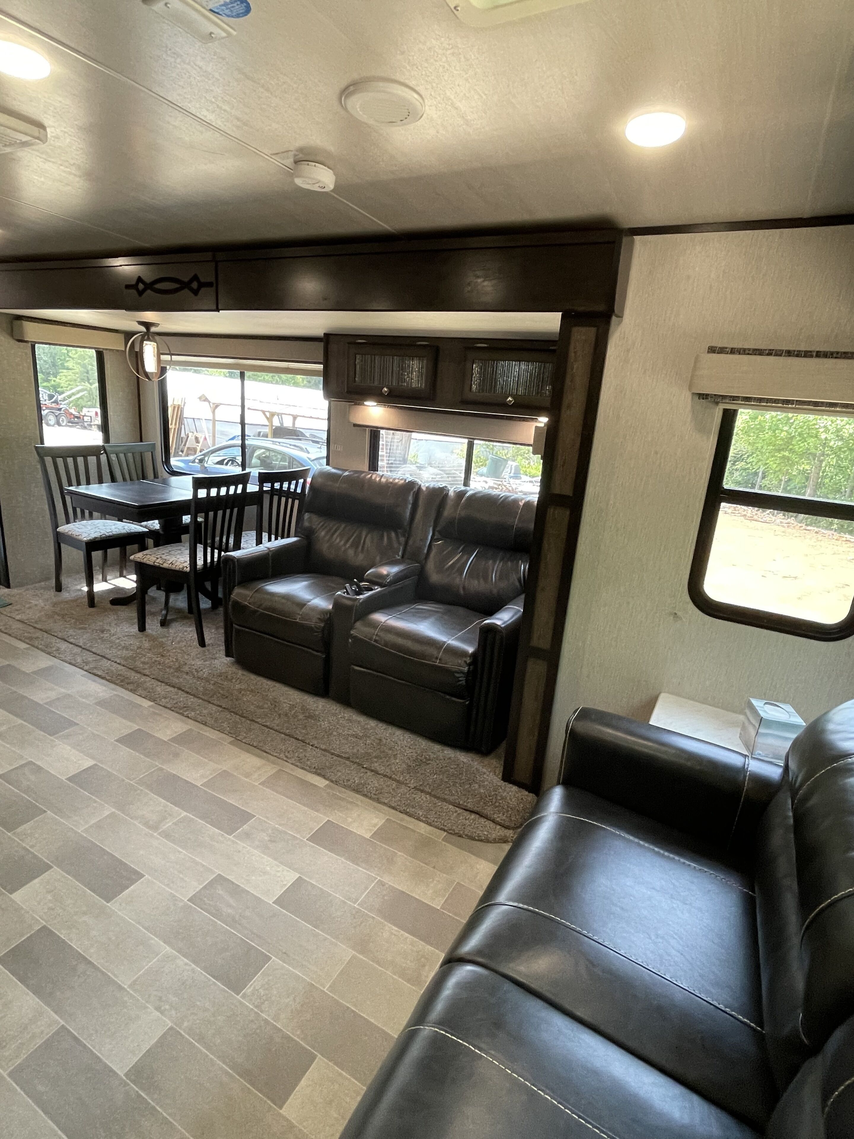 A compact RV interior with a dining area, two leather sofas, and a small table.