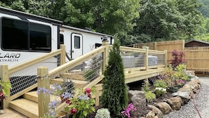A campsite with a white RV, wooden steps, and a garden with flowers and rocks. - Farm Glamping @ The Sage Getaway RV (Hot Springs)