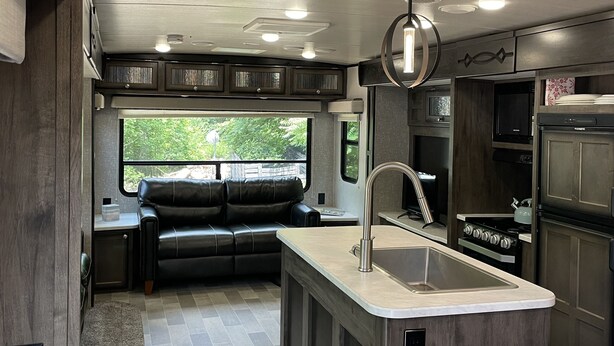 A compact RV kitchen with a central island, built-in appliances, and a view through a window. - Farm Glamping @ The Sage Getaway RV (Hot Springs)