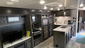 A modern kitchen with built-in appliances, a large TV, and a central island. - Farm Glamping @ The Sage Getaway RV (Hot Springs)