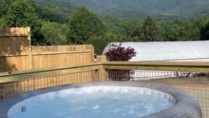 A hot tub with a wicker design, surrounded by a wooden fence and a view of green mountains. - Farm Glamping @ The Sage Getaway RV (Hot Springs)