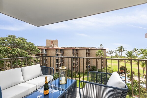Un balcon avec un canapé, une table avec une bouteille et un verre, et une vue sur un immeuble doté de nombreux balcons et de palmiers.