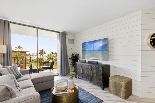 A modern living room with a large TV, grey sofa, and a view of the outdoors.