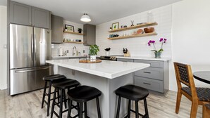 A modern kitchen with a large island, stainless steel appliances, and bar stools. - Aloha Chic Penthouse Vistas (Kihei)