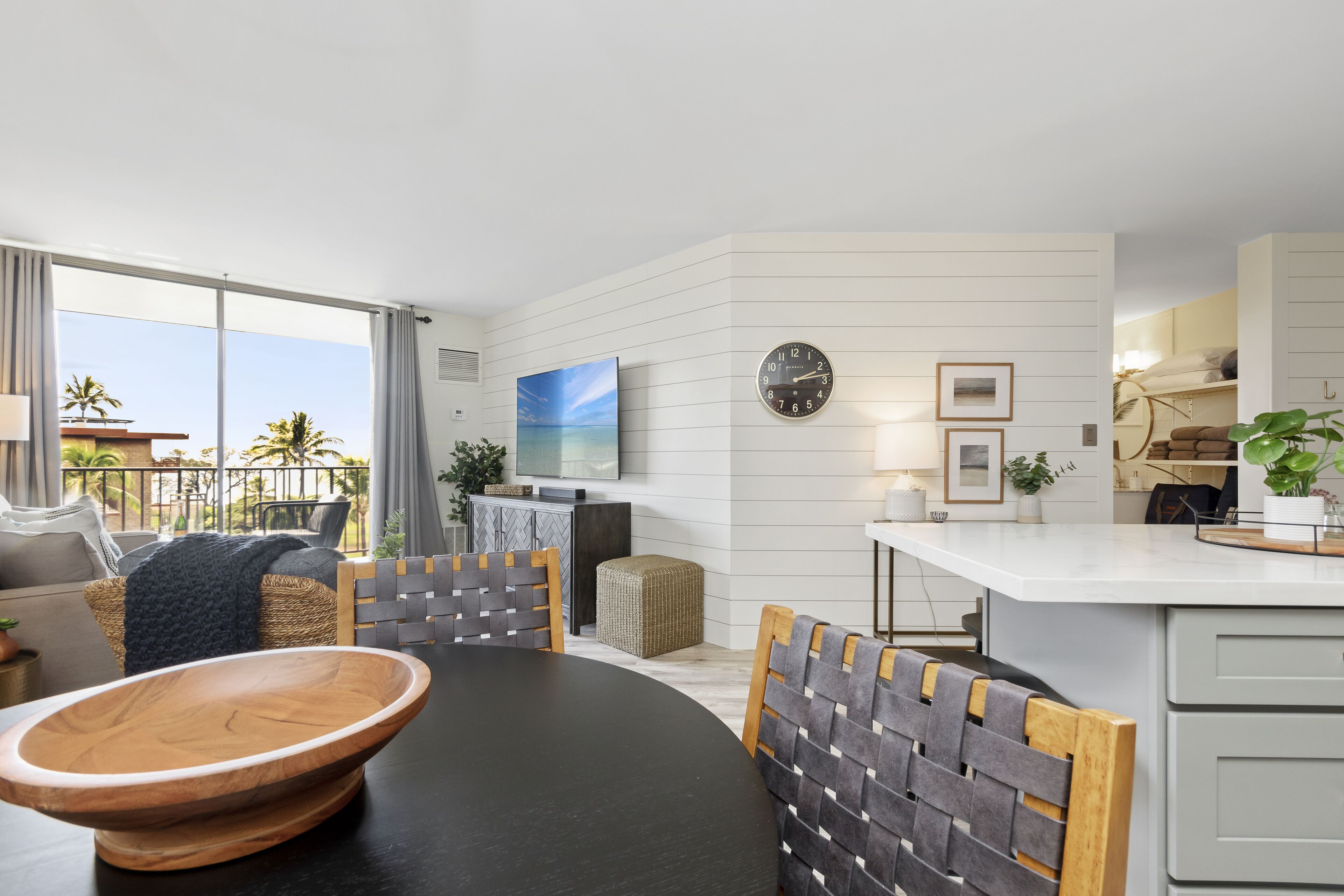 A modern kitchen with a dining area, featuring a large island, a television, and a clock on the wall.