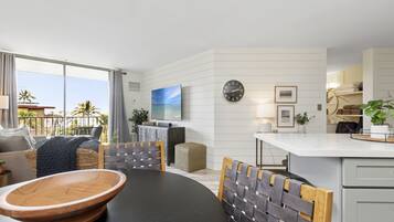 A modern kitchen with a dining area, featuring a large island, a television, and a clock on the wall.