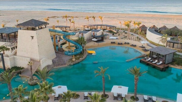 Un complexe hôtelier doté d’une piscine centrale, d’un toboggan aquatique et offrant une vue sur la plage.