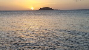 A sunset over a calm sea with a distant island. - Bungalow Saphir Idéal Pour Amoureux à 2 Minutes de la Plage, en Bord de Piscine! (Sainte-Rose)