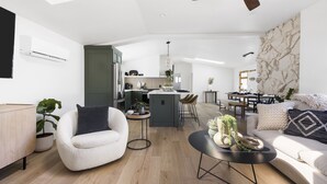 Ein modernes Wohnzimmer mit Sofa, Sessel und Couchtisch. Es gibt eine Küchenzeile mit Esstisch und Stühlen.