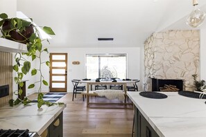 A modern kitchen with a central island, wooden flooring, and a dining area with a large window. - Stunning Sedona Modern Bungalow | Private Spa-Style Backyard | EV Charger (Sedona)