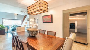 A spacious dining area with a wooden table, chairs, and a large woven bowl centerpiece. A modern chandelier hangs above, and a stainless steel refrigerator is visible in the background. - Penthouse w Jacuzzi and Ocean View Puerto Bahia (Samaná)