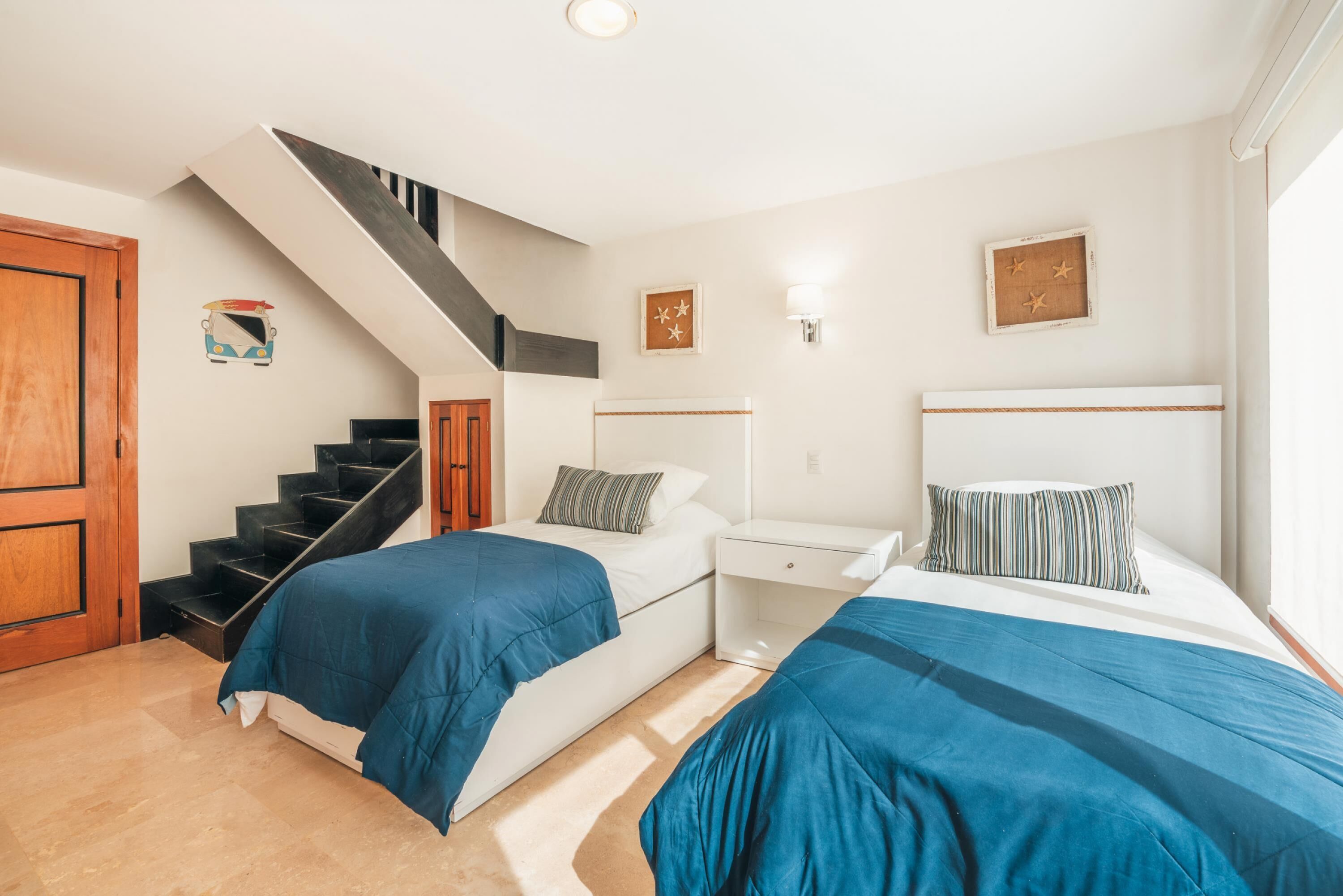 A bedroom with two beds, a staircase, a nightstand, and a wall-mounted light fixture.