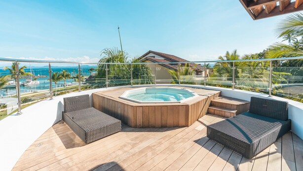 A wooden deck with a hot tub, seating, and a view of the sea. - Penthouse w Jacuzzi and Ocean View Puerto Bahia (Samaná)