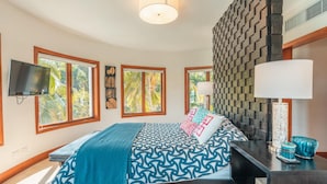 A bedroom with a bed, a TV, a window, a wall with a geometric pattern, and a lamp. - Penthouse w Jacuzzi and Ocean View Puerto Bahia (Samaná)
