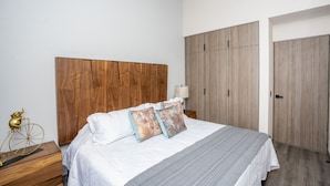 Quarto com cabeceira de madeira, cama com almofadas estampadas, abajur e dois armários.