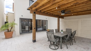 Um pátio externo com pérgola de madeira, uma mesa com cadeiras e um vaso de planta.