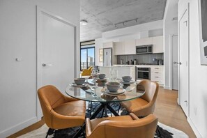 Une cuisine moderne avec des meubles blancs, un four à micro-ondes et un coin repas comprenant une table en verre et des chaises en cuir.