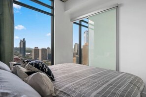 Une chambre avec une grande fenêtre, un lit avec une literie à rayures et une vue sur la ville.