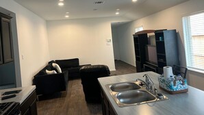 Una cocina moderna con un lavamanos doble, un comedor con un sofá negro y una estantería empotrada.