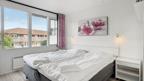 Ein Schlafzimmer mit einem großen Bett, einem Fenster mit Vorhängen, einem Wandbild und einem Nachttisch.
