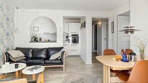Ein modernes Wohnzimmer mit einer schwarzen Ledersofa, einem weißen Couchtisch und einem Essbereich mit einem Holztisch und orangefarbenen Stühlen.