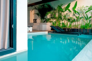 A modern indoor pool with clear blue water, surrounded by lush green plants and a minimalist seating area. - Green Flow Villa 3 (Ubud)