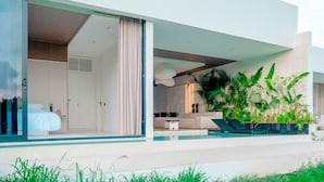 A modern house with a large glass door leading to a bedroom, a living area with a sofa and a coffee table, and a pool area with lounge chairs. - Green Flow Villa 3 (Ubud)