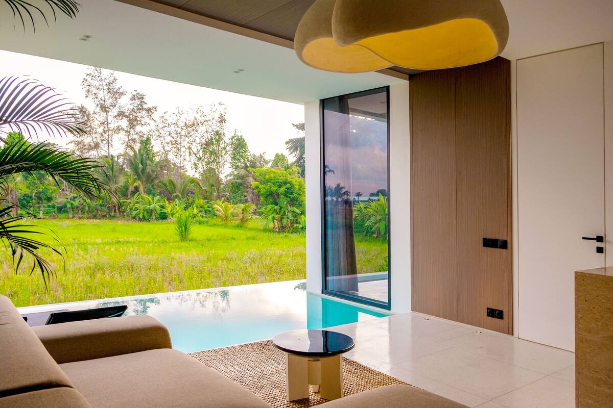 A modern living room with a glass door leading to a pool, surrounded by lush greenery.