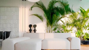 A modern living room with a sectional sofa, a geometric patterned wall, and large green plants. - Green Flow Villa 3 (Ubud)