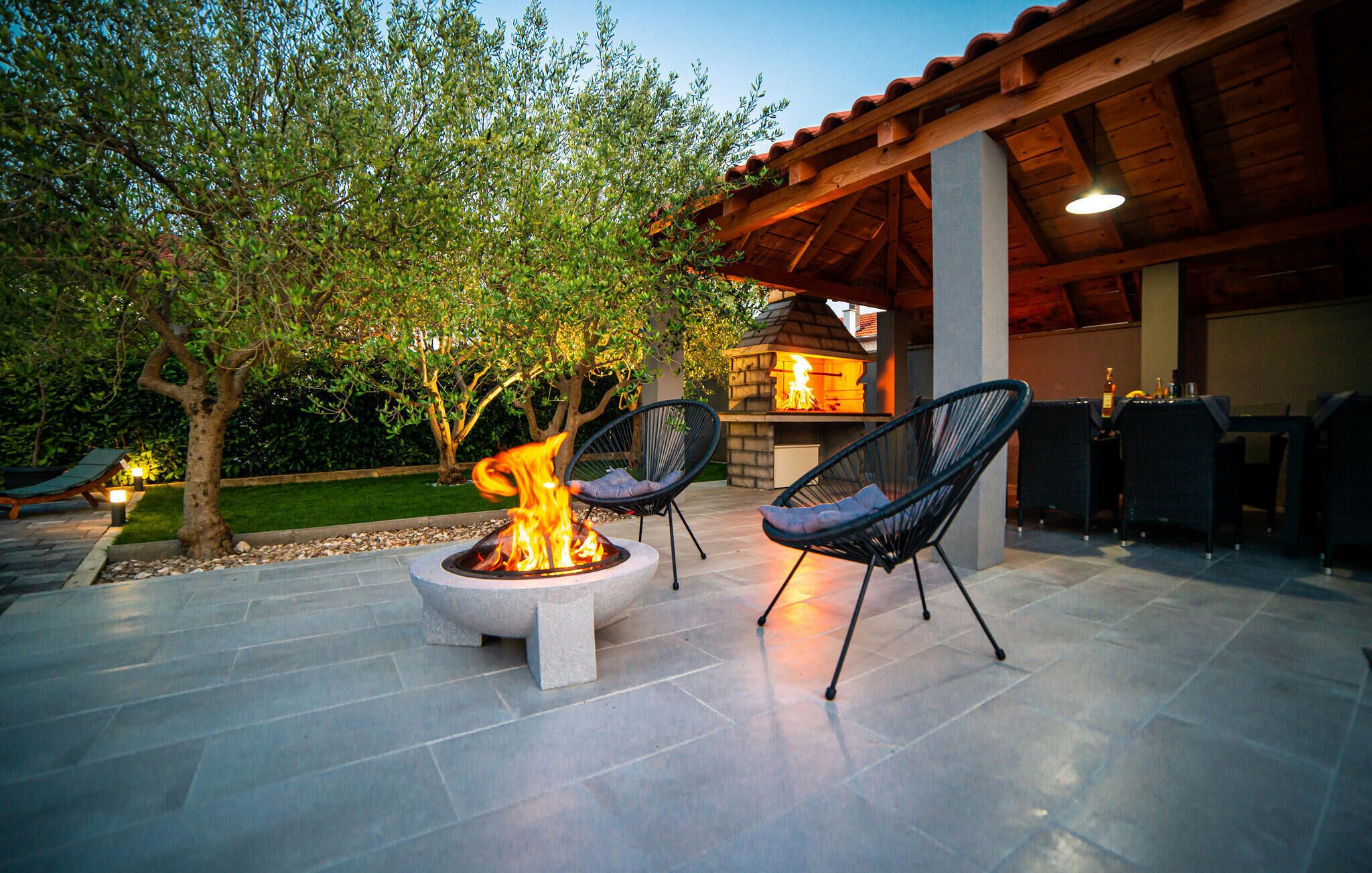 An outdoor patio with a fire pit, two lounge chairs, and a stone barbecue grill.