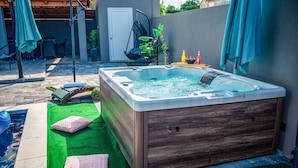 A hot tub with a wooden exterior, surrounded by a patio with green artificial grass, a small pool, and a swing chair. - Beautiful home in Polaca (Polaca)