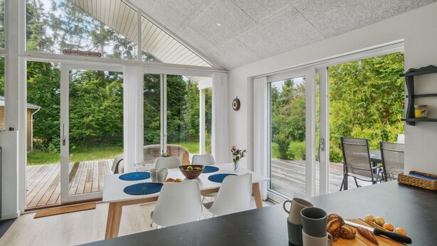 A modern kitchen with large sliding glass doors, a dining area with white chairs and blue placemats, and a view of a lush garden. - Stunning home in Jægerspris with WiFi (Jægerspris)