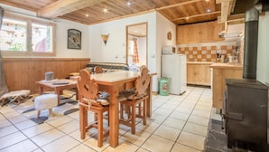 L’intérieur chaleureux d’un chalet avec une table à manger en bois, des chaises, un coin cuisine équipé d’une cuisinière et une grande fenêtre.