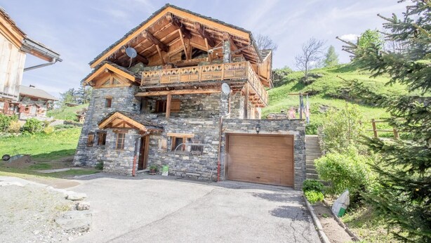 Une maison en pierre à deux étages, dotée d’un balcon en bois, d’un garage et d’une allée.