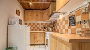 Une cuisine compacte avec des meubles en bois, un réfrigérateur blanc, un pare-feu en carreaux et un étendoir suspendu.