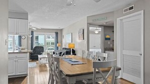 A spacious living area with a dining table, chairs, a sofa, and a ceiling fan. - First Floor Pebble Beach
3BR/2BA Oceanview Condo 
Steps from the Beach
 (Emerald Isle)