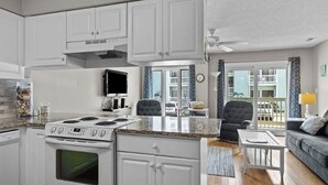 A compact kitchen with white cabinets, a stove, and a dining area with a table and chairs. - First Floor Pebble Beach
3BR/2BA Oceanview Condo 
Steps from the Beach
 (Emerald Isle)