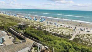 A beach with a wooden boardwalk, beach umbrellas, and a clear view of the ocean. - First Floor Pebble Beach
3BR/2BA Oceanview Condo 
Steps from the Beach
 (Emerald Isle)