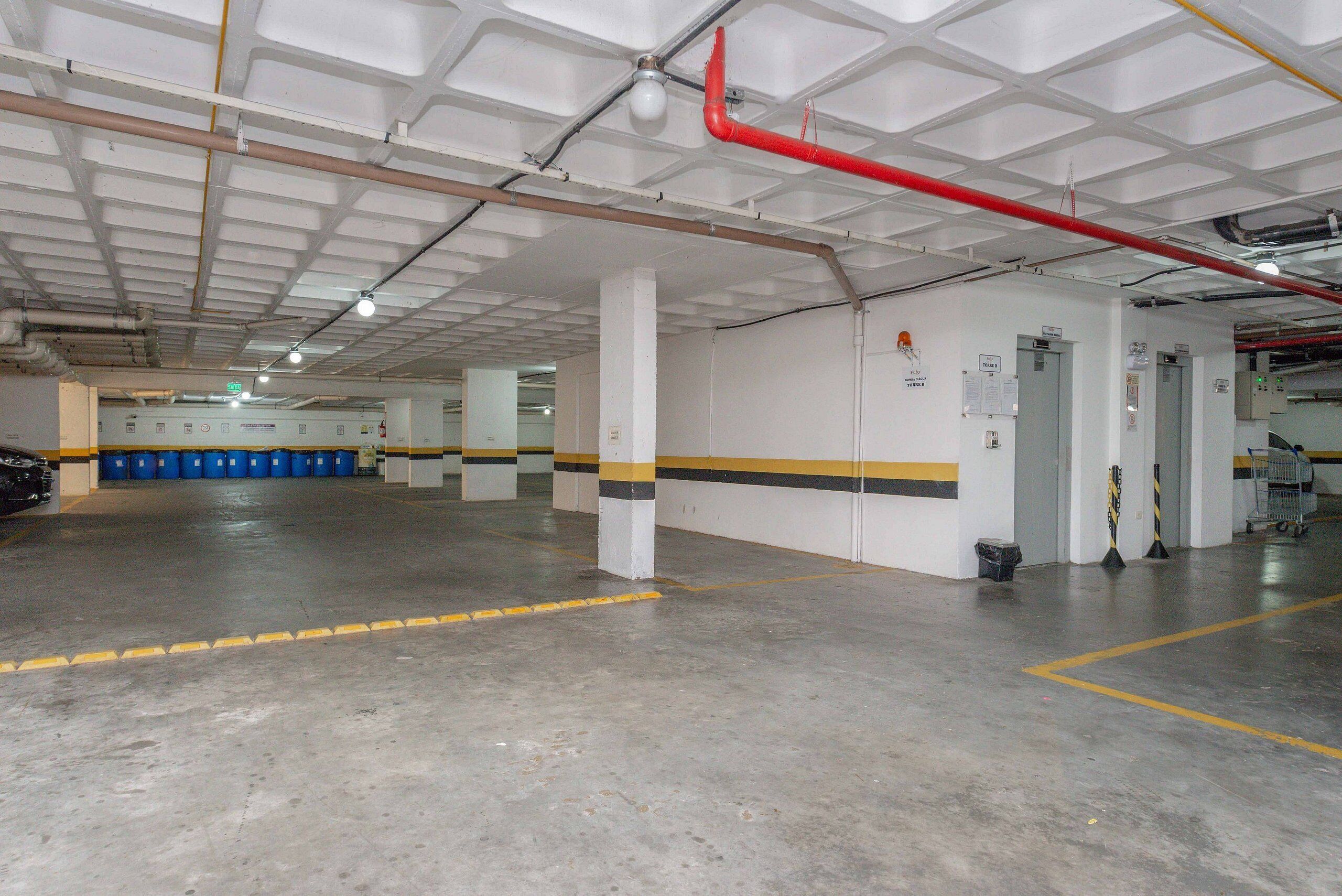 Un vaste espace de stationnement intérieur doté d’un sol en béton, de murs blancs et de colonnes à rayures jaunes et noires.