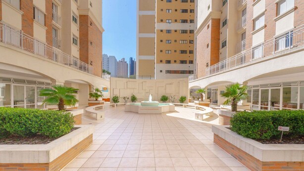 A courtyard with a central fountain, surrounded by planters and buildings with balconies. - Condominio Felice (Curitiba)